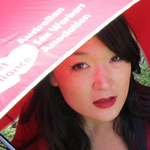 photo of jules kim looking up at the camera from under a red umbrella wearing red lipstick