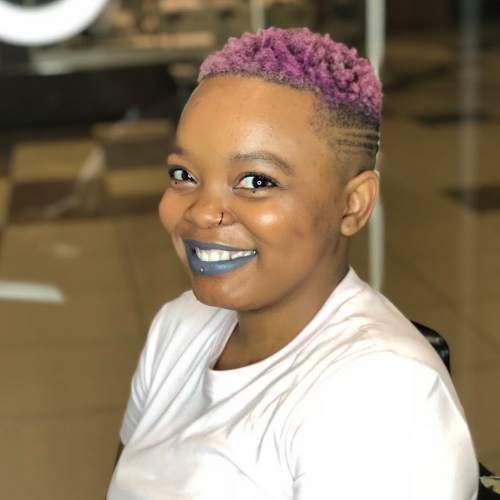 Head and shoulders of Tsehgofatsa Senne in a white shirt with purple hair and blue lipstick