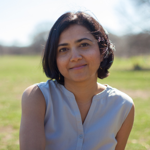 Vaishali Sinha headshot with blurry natural green scene behind